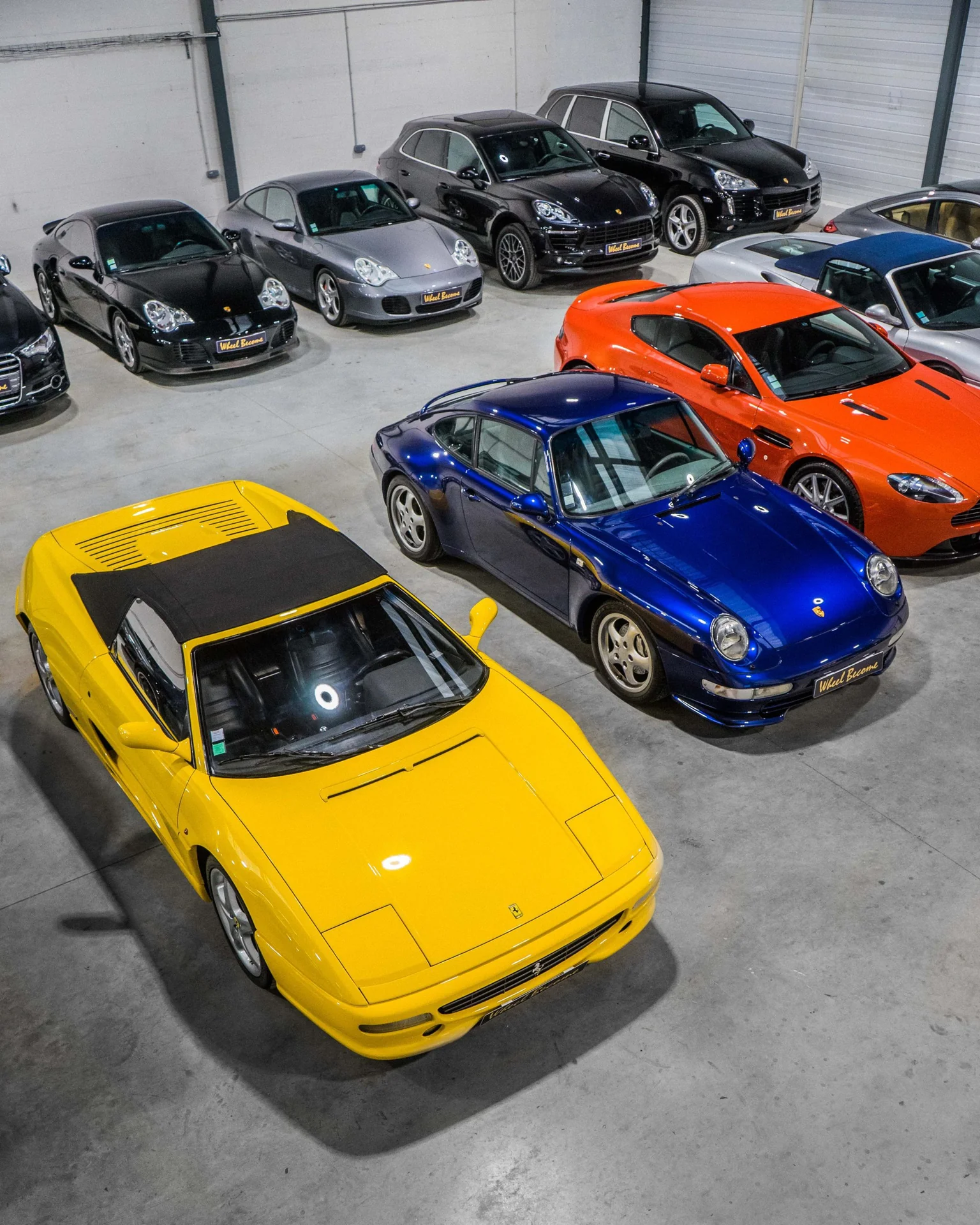 Vue du showroom Wheel Become avec une Ferrari jaune, une Porsche 911 bleue et des voitures de sport. Photo : Wheel Become.